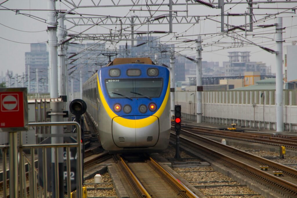 A sleek train approaches a station in a bustling Taiwanese city, showcasing modern rail technology.